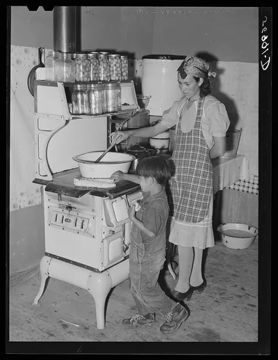 Spanish-American woman stirring pan of cooking beans. Small boy is…, New Mexico, 1940