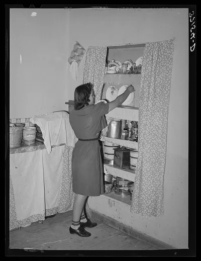 Daughter of Spanish-American putting dishes into cupboard. Chamisal,…, New Mexico, 1940